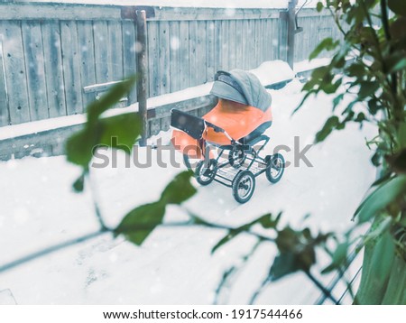 Baby stroller on the street. View through the window from the house with flowers on the windowsill.