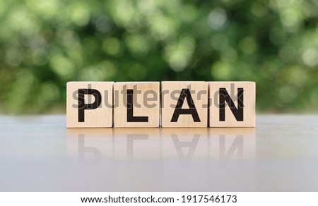 PLAN word written on wooden blocks. The text is written in black letters and is reflected in the mirror surface of the table. Business concept for your design.