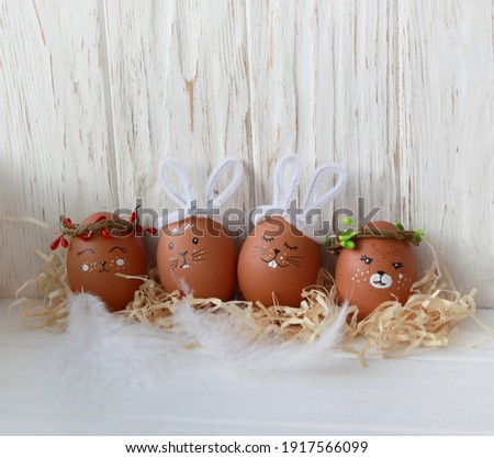 Easter eggs with animal muzzles on a white wooden background with feathers and straw, Easter bunnies and other hand-drawn animals, Easter decor from natural materials, do it yourself