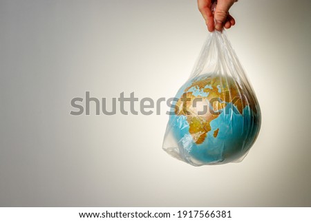 The concept of World Environment Day. The man's hand holds the earth in a plastic bag. In the blank for social advertising there is a place for the inscription. Royalty-Free Stock Photo #1917566381