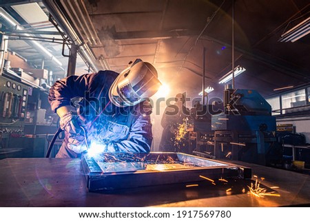 The two handymen performing welding and grinding at their workplace in the workshop, while the sparks "fly" all around them, they wear a protective helmet and equipment. Royalty-Free Stock Photo #1917569780