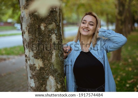 A young blonde lady with denim jacket posing for the camera in the autumn park