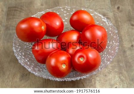 Heap of tomatoes on a transparent glass bowl over a wood table