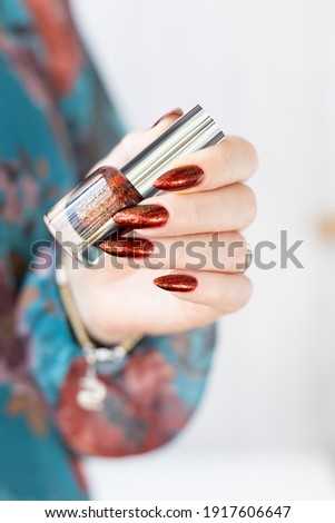 Female hand with long nails and golden brown maroon, manicure holds a bottle of nail polish