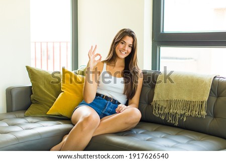 young pretty woman feeling happy, relaxed and satisfied, showing approval with okay gesture, smiling