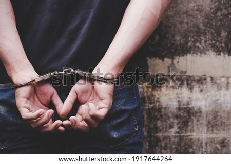Thief under arrest and get cuffed by policeman Bad person stand against wall, get hand crossed back with handcuffs Murderer is criminal person He can be cyber crime Human trafficking Criminal concept Royalty-Free Stock Photo #1917644264