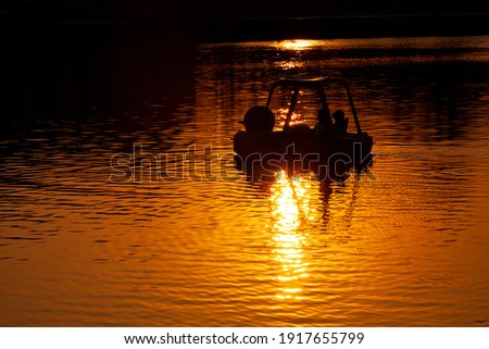 Silhouette of tourists playing a pedal boat on the river during the sunset.