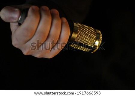 A hand holding a condenser microphone with a black background