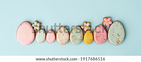 Sweets, pastry, gingerbread cookies for Easter table. Easter eggs and tender simple flowers on blue background top view copy space, spring seasonal holiday banner for your sute, flyer, coupon