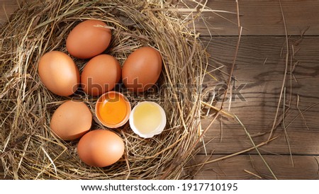 Several raw fresh chicken eggs in a nest of hay on a wooden background, horizontal banner