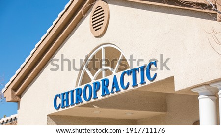 A chiropractic office in Las Vegas, NV, USA. Grainy stucco texture on the wall with tiled roof. Clear blue sky in the background.