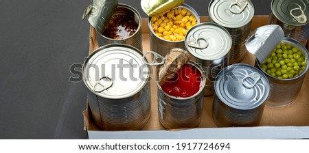 Caned vegetables such as beans, peas, corn, tomatos in cardboard box. Tin cans. Dark background. Copy space, panorama banner Royalty-Free Stock Photo #1917724694