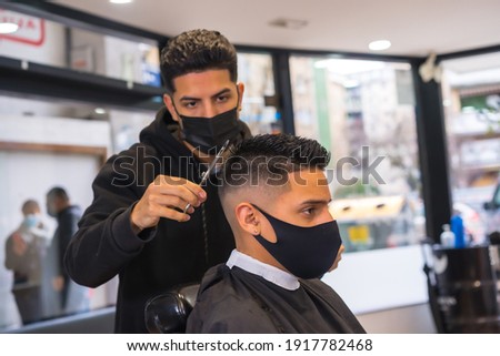 Hairdresser with face mask finishing the cut to the client. New normality of Hairdressers in the Covid-19 pandemic Royalty-Free Stock Photo #1917782468