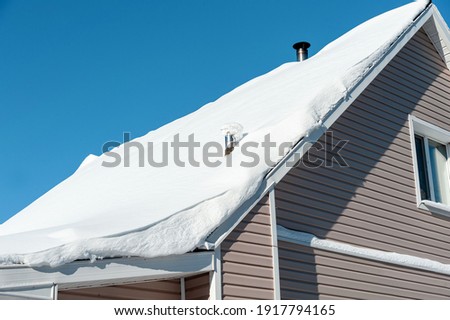 A lot of snow on the roof of a private house, blue sky on a frosty day
