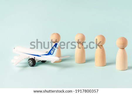 Wooden figures of people stand in line to board the plane, observing the distance