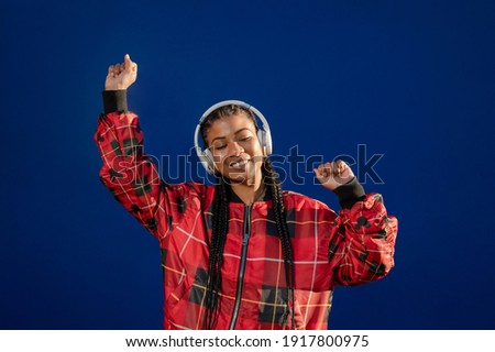 A beautiful Afro-American female listening and enjoying music with headphones on blue background