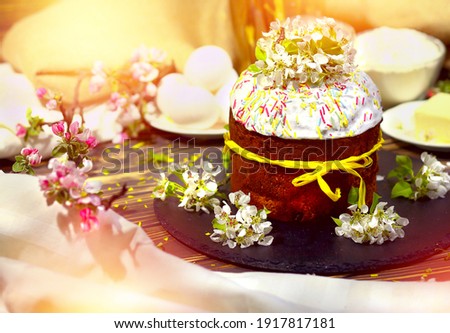 Easter cake with a yellow ribbon on the table. Wooden board brown background. The decor on the table is apple-tree flowers and ingredients. Sun rays, boke and flash background