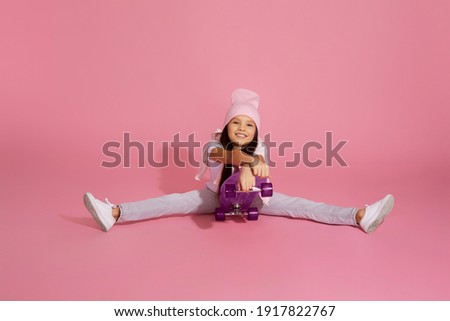 happy cute little child girl on skateboard having fun over pink background.