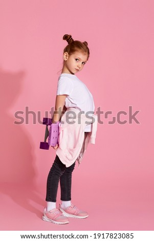 adorable little child girl with skateboard over pink background. side view.