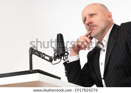 A thoughtful man sits next to the microphone. The man and the microphone are taken from below. Lecturer in front of a microphone on a white background.