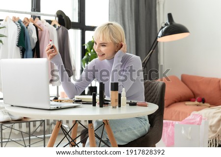 A cute young blonde woman online shows red lipstick, teaches make-up in her masterclass on the application of zoom in a laptop computer. Charming girl blogger communicates through app