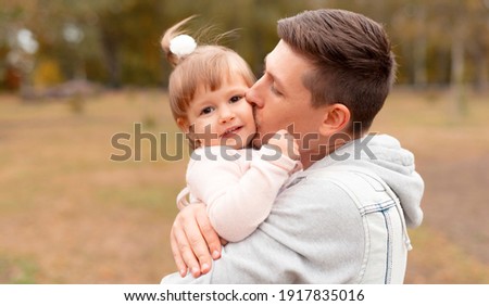 Cheerful young father kissing his little cute daughter outdoor.