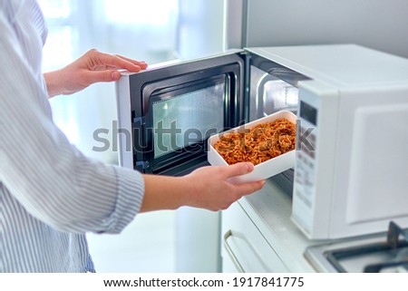 Female hands warming up a container of food in the modern microwave oven for snack lunch at home  Royalty-Free Stock Photo #1917841775
