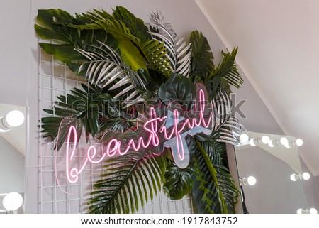 Pink shining neon inscription Beautiful on artificial tropic plant leaves, room interior decoration, lights bokeh, mirror on background.