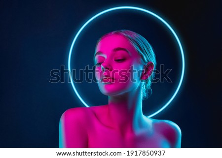 Future. Portrait of female fashion model in neon light with neoned blue glowing circle on dark studio background. Beautiful woman with trendy make-up and well-kept skin. Vivid style, beauty concept. Royalty-Free Stock Photo #1917850937