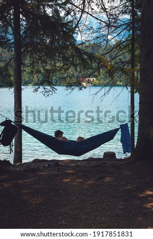 Silhouette of a man lie in the hammock near the lake. Calm, around the forest, silhouettes of trees, pine. Bled, Slovenia. Vertical photo