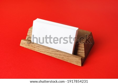 Blank business cards on wooden holder at red paper background. Responsive design mockup.