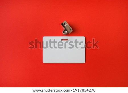 Photo of blank white plastic badge on red paper background. Blank id card. Top view. Flat lay.