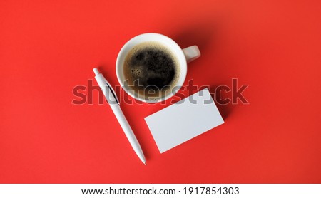 Blank business cards, coffee cup and pen on red paper background. Top view. Flat lay.