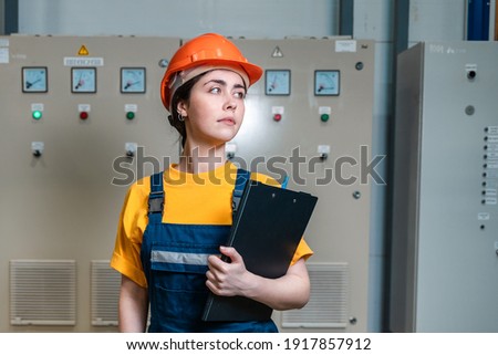Production inspection. Portrait of female worker in a uniform and a protective helmet, holding a folder.