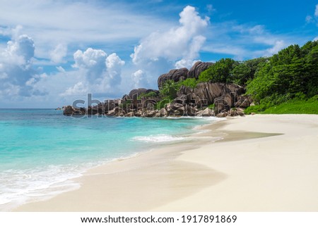 Grand Anse Beach on La Digue Island in Seychelles. The picture shows turquoise water with tropical sandy beaches and green foliage. 
