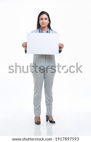 Excited mature woman holding empty white board over white background.
