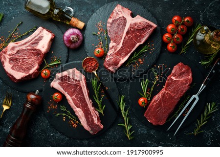 Set of raw steaks - t-bone, tomahawk, striploin, tenderloin, new york steak. On a black stone background. Top view. Royalty-Free Stock Photo #1917900995