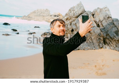 Middle aged man making selfiie, video calling in the waterfront. De focused face. Selective focus on hand
