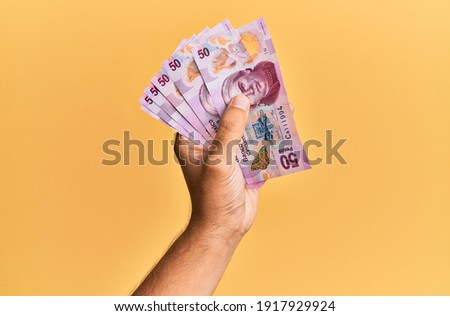 Hand of hispanic man holding mexican 50 pesos banknotes over isolated yellow background.