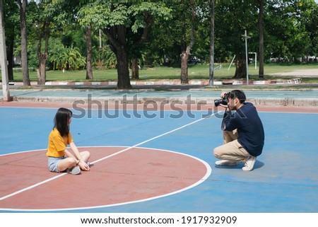 Male photographer take a photo of girl model while standing, jumping and sitting in the basketball court.