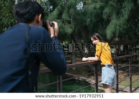 Male photographer take a photo of teenage female model while she standing and sitting on the small bridge in the park.