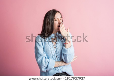 Exhausted brunette girl yawns in studio on pink background