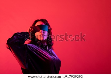 Young girl wearing galactic glasses and headphones with her arm behind her head, against red background