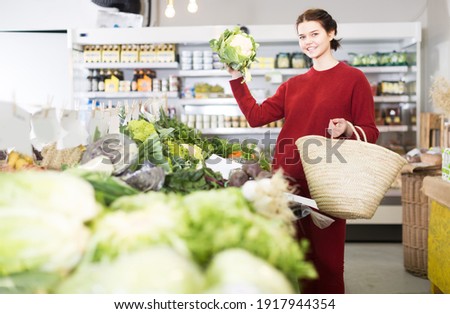 Smiling girl showing fresh cauliflower in vegetable department of store