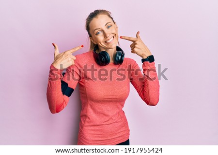 Beautiful caucasian woman wearing sportswear and arm band smiling cheerful showing and pointing with fingers teeth and mouth. dental health concept. 