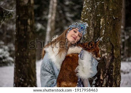 beautiful russian girl in national costume with a red fox in the winter forest 