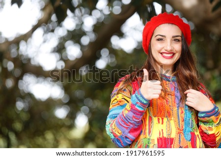 portrait of beautiful white girl with colorful sweater and red headphone, isolated on nature background making the ok sign with her fingers