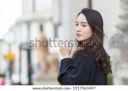 A picture of a beautiful long haired Asian woman in a black robe walking and looking out in the city outdoors.