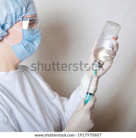A nurse fills a syringe with medicine from a bottle. Close-up. A nurse on a white background in a protective uniform, wearing gloves and a mask. The operating unit.
