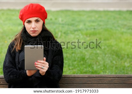 girl dressed in black with a red headset uses her tablet sitting in a bench in a park